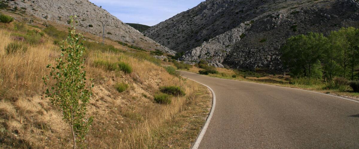A winding mountain road with rocky terrain and sparse vegetation.