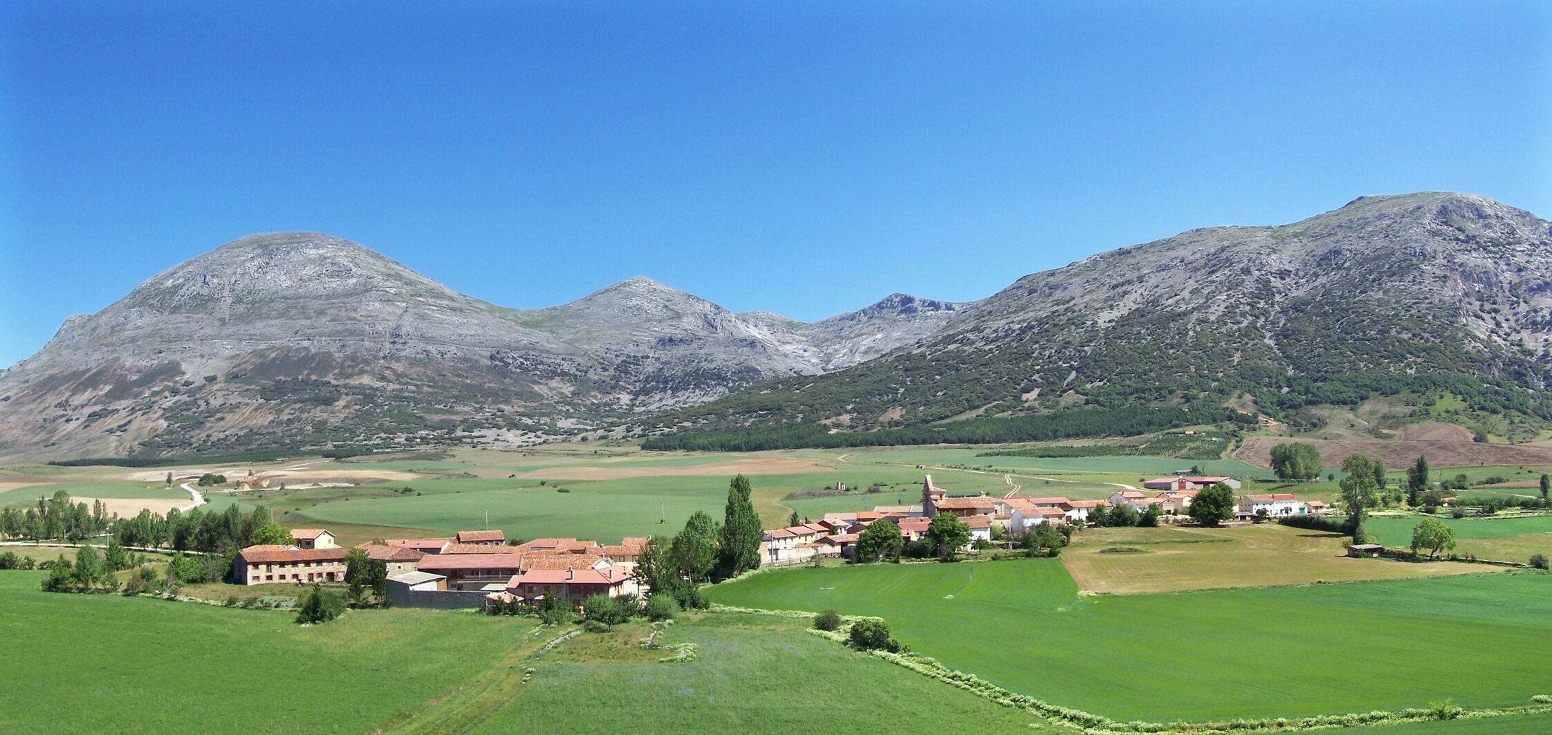 A rural village with houses and fields, surrounded by mountains.