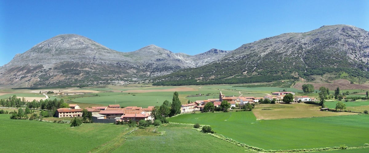 A rural village with houses and fields, surrounded by mountains.