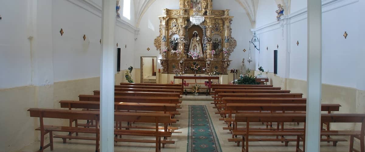 An ornate church interior with a central altar, wooden pews, and a green carpet leading to it.