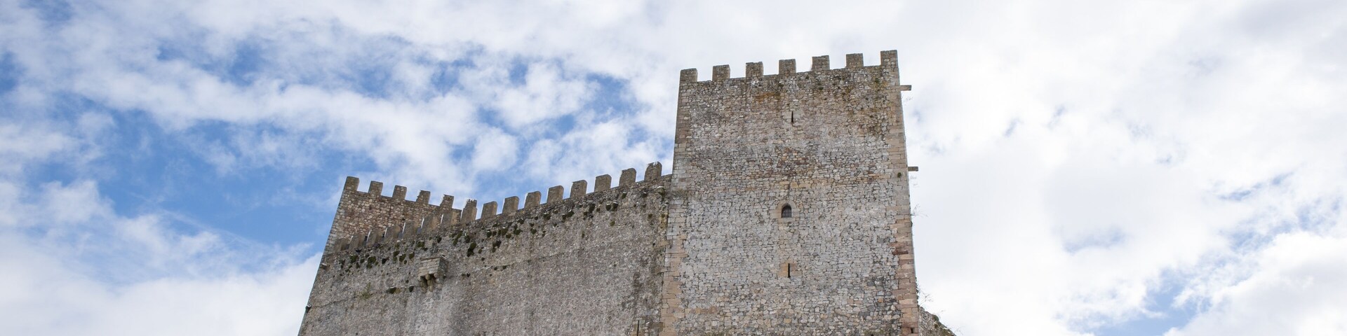 A medieval stone castle on a snow-covered hill under a partly cloudy sky.