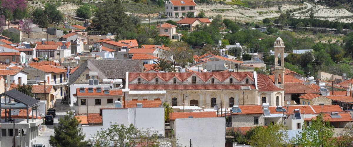 A coastal town with terracotta-roofed buildings, a prominent church with a bell tower, and a hilly backdrop.