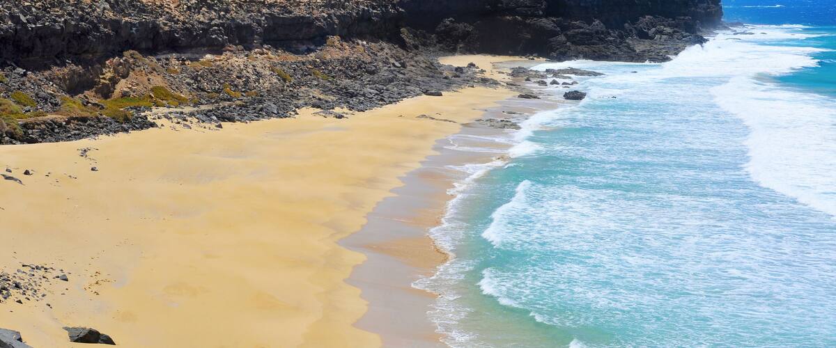 A coastal landscape with a sandy beach, rocky cliffs, and ocean waves.