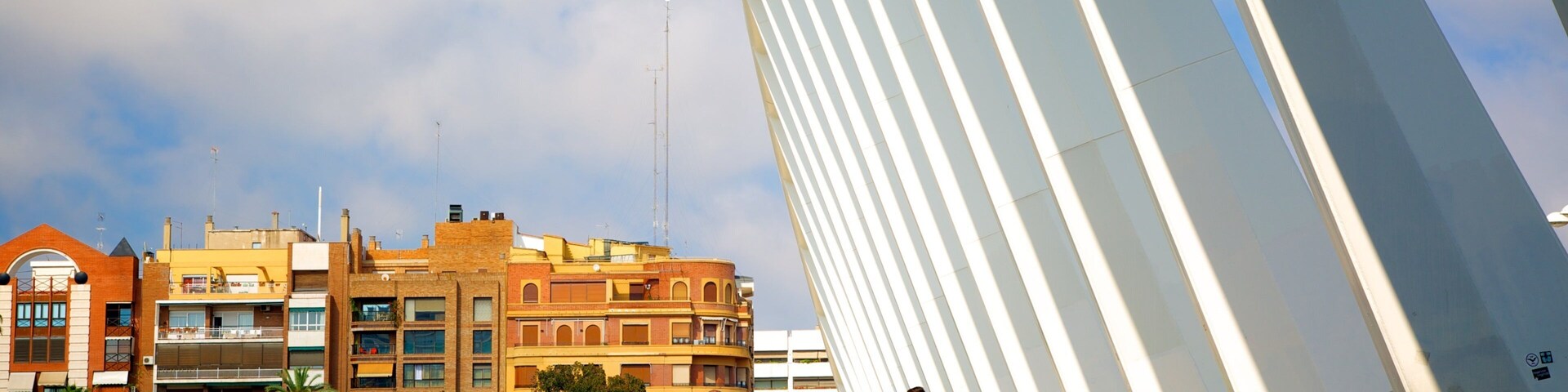 A modern bridge with white railings and a curved walkway. In the background, there are multi-story buildings with a mix of architectural styles.