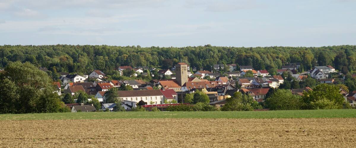 A rural village with houses, a church, and a forested hill in the background.