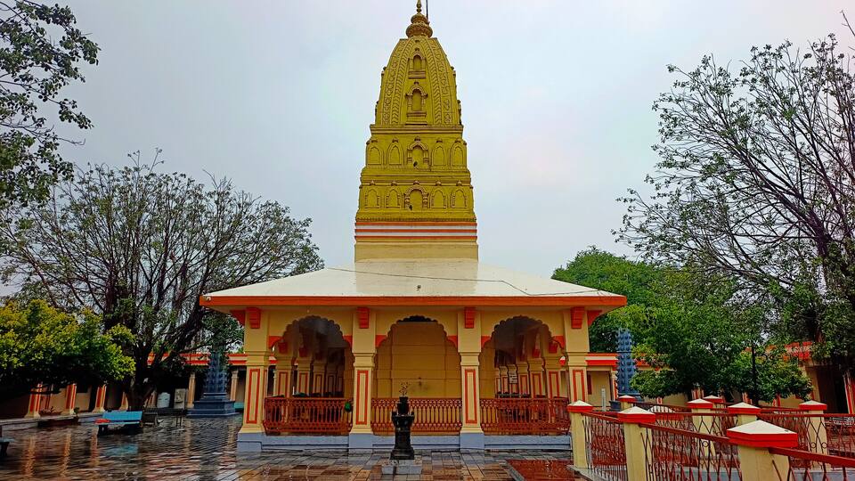 A yellow temple with a spire, surrounded by trees and a tiled courtyard.