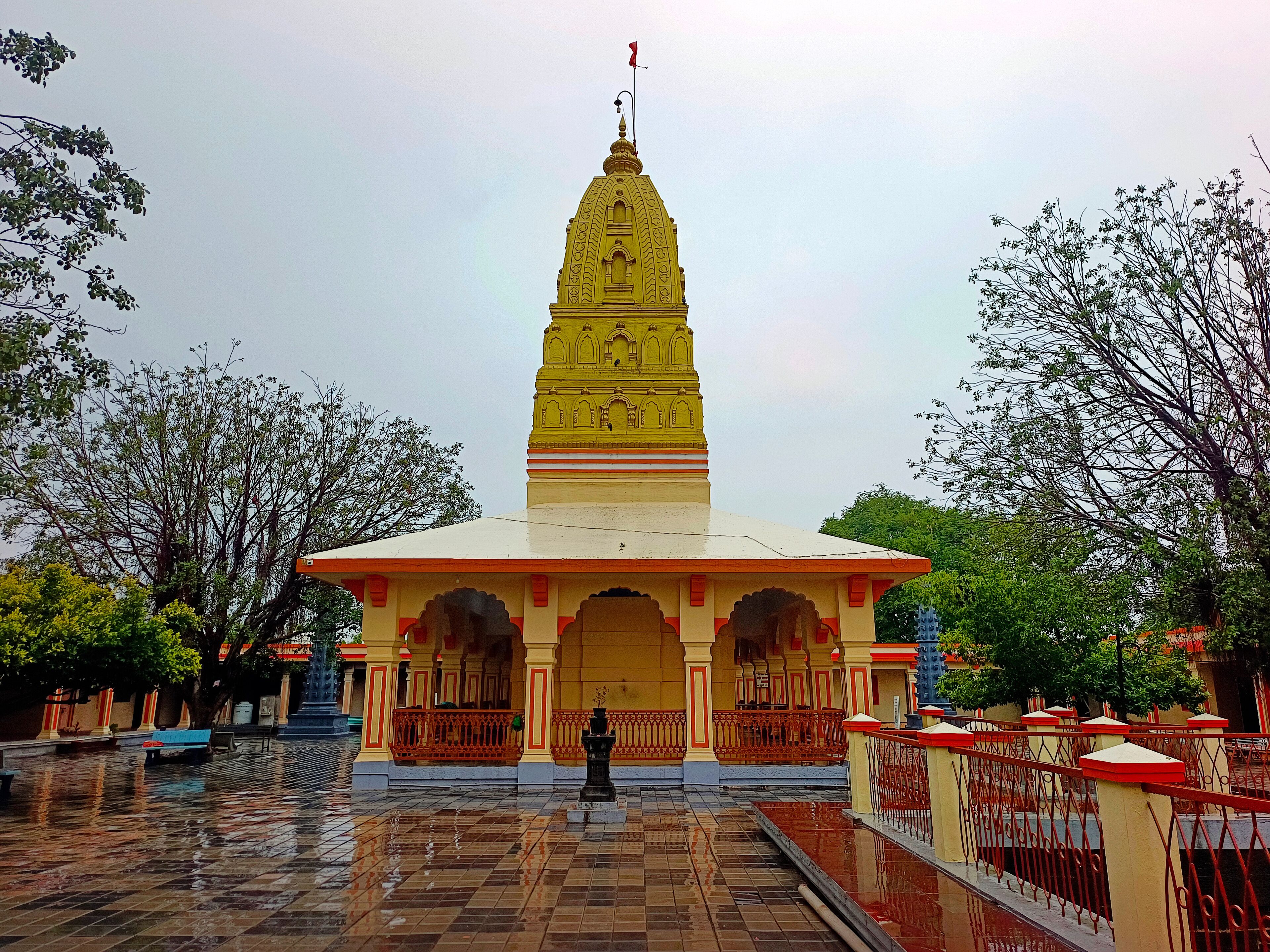 A yellow temple with a spire, surrounded by trees and a tiled courtyard.