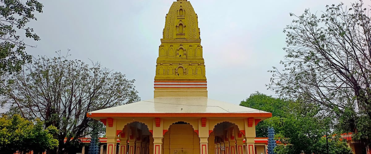 A yellow temple with a spire, surrounded by trees and a tiled courtyard.