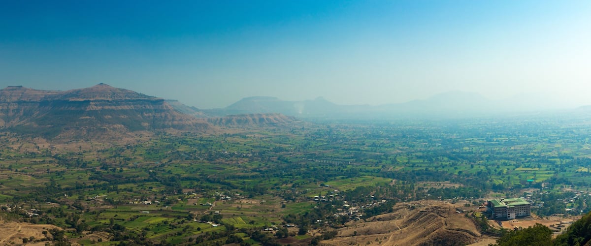 A panoramic view of a valley with rolling hills, a river, and scattered buildings.
