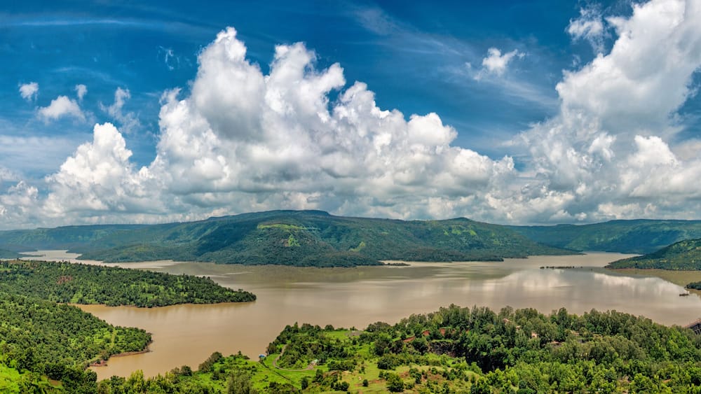A river surrounded by lush green hills and a cloudy sky.