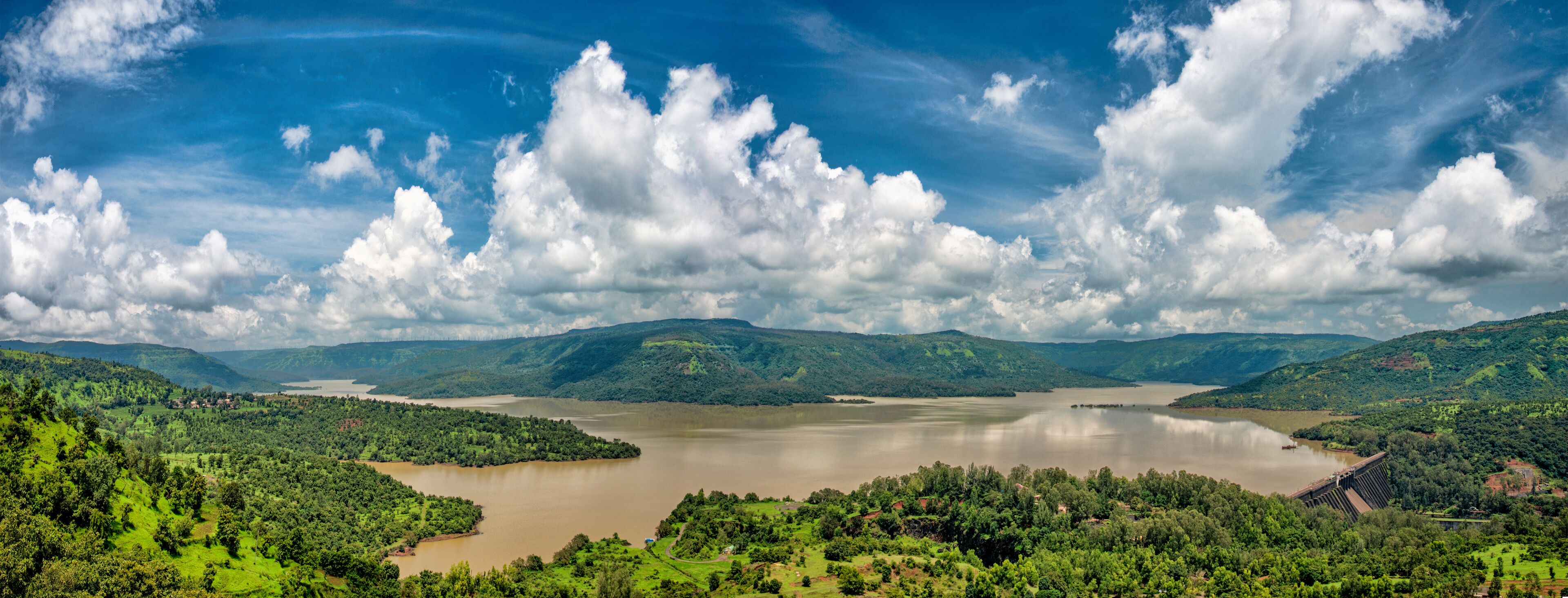 A river surrounded by lush green hills and a cloudy sky.