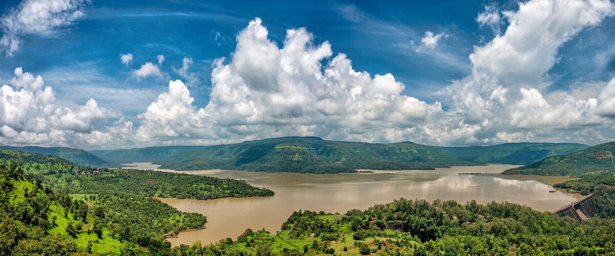 A river surrounded by lush green hills and a cloudy sky.