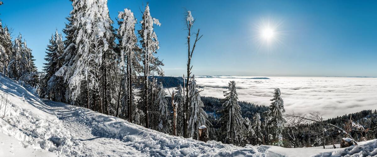 A snow-covered mountain landscape with a clear sky and a sun shining through the clouds.