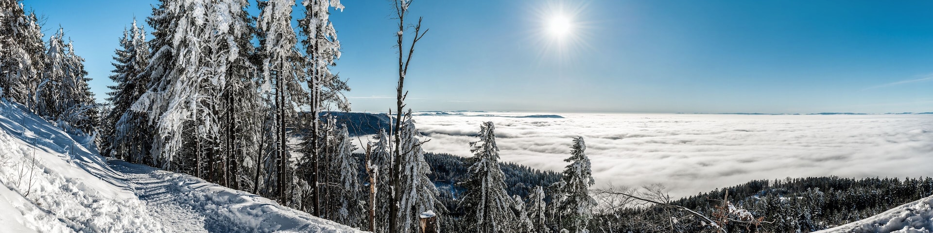 A snow-covered mountain landscape with a clear sky and a sun shining through the clouds.