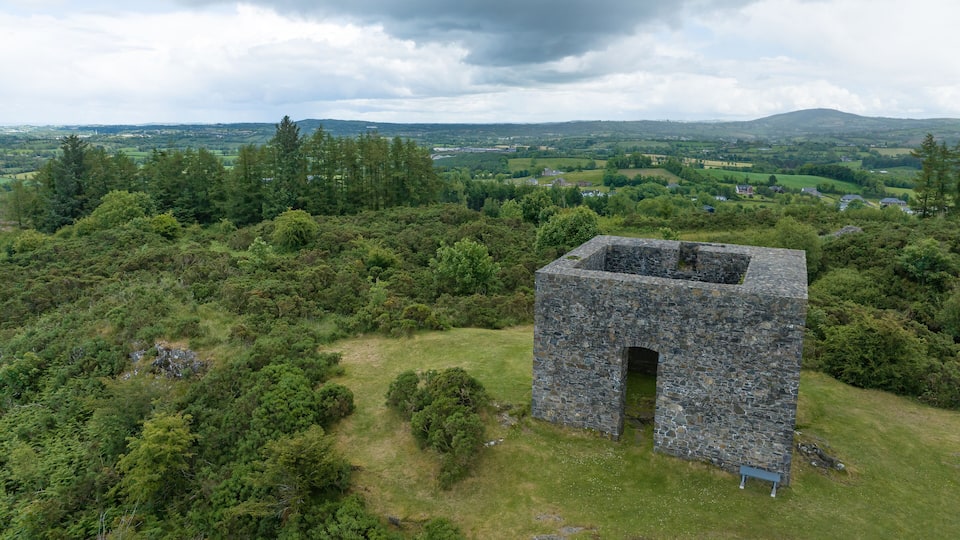 A stone structure in a grassy area with a view of a hilly landscape and distant buildings.