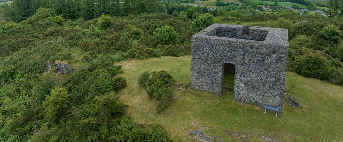 A stone structure in a grassy area with a view of a hilly landscape and distant buildings.