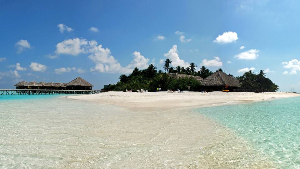 A beach with clear turquoise water, a sandy shore, and overwater bungalows.