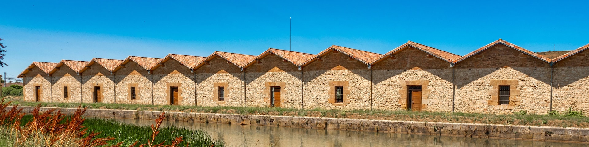 Filas de edificios de piedra con tejados de baldosas junto a una masa de agua tranquila.