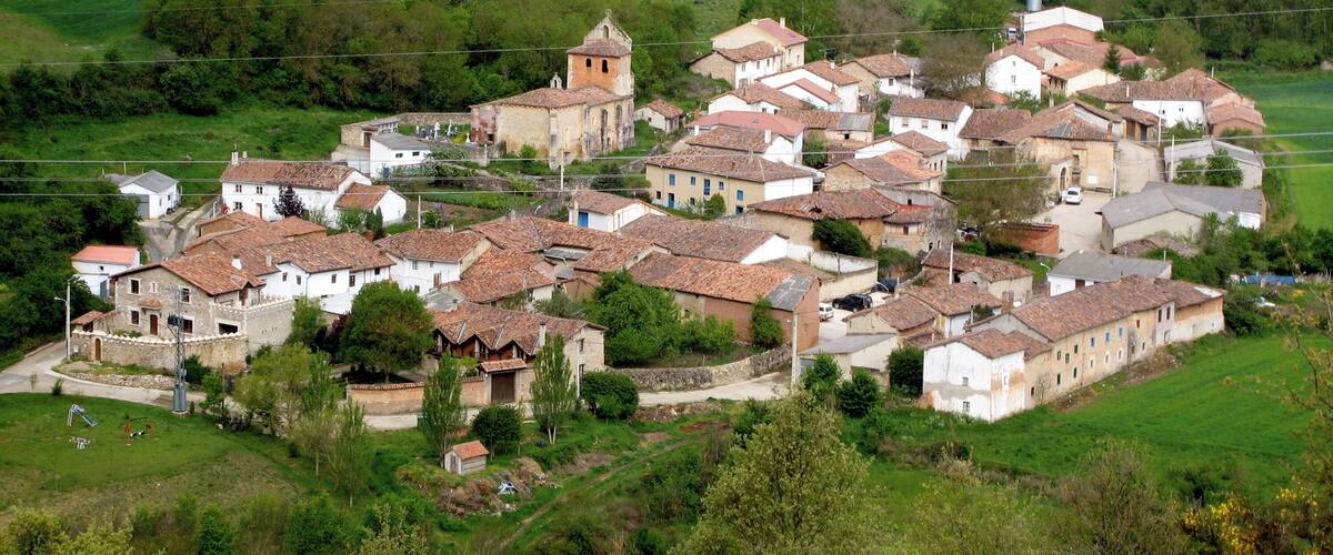 A village with terracotta-roofed houses, a church with a bell tower, and surrounding green fields.