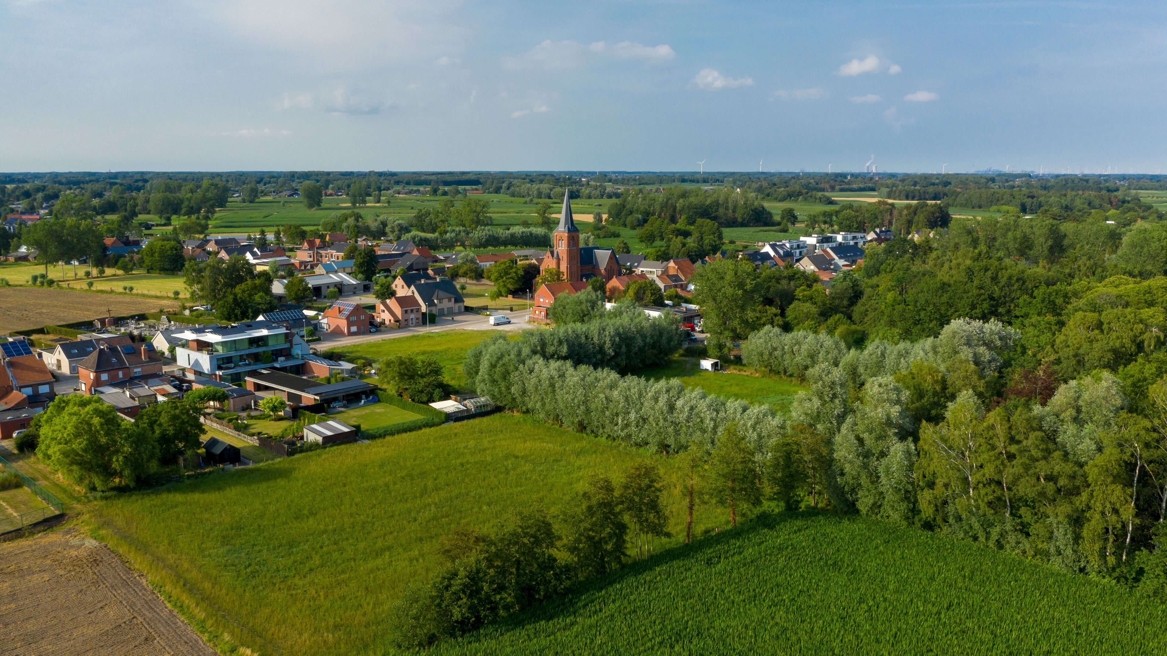 A rural landscape with a church, residential houses, and wind turbines in the distance.
