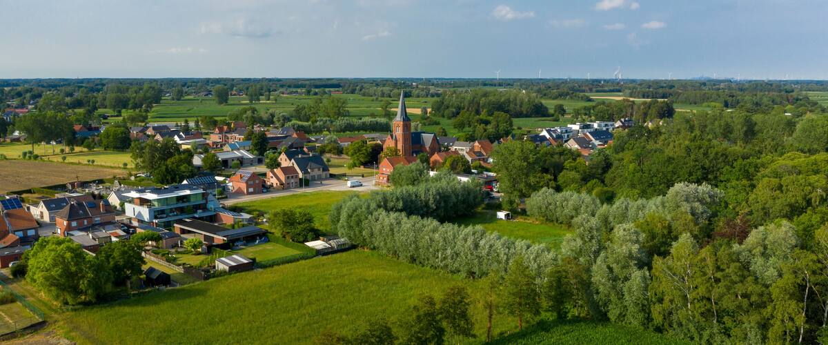 A rural landscape with a church, residential houses, and wind turbines in the distance.