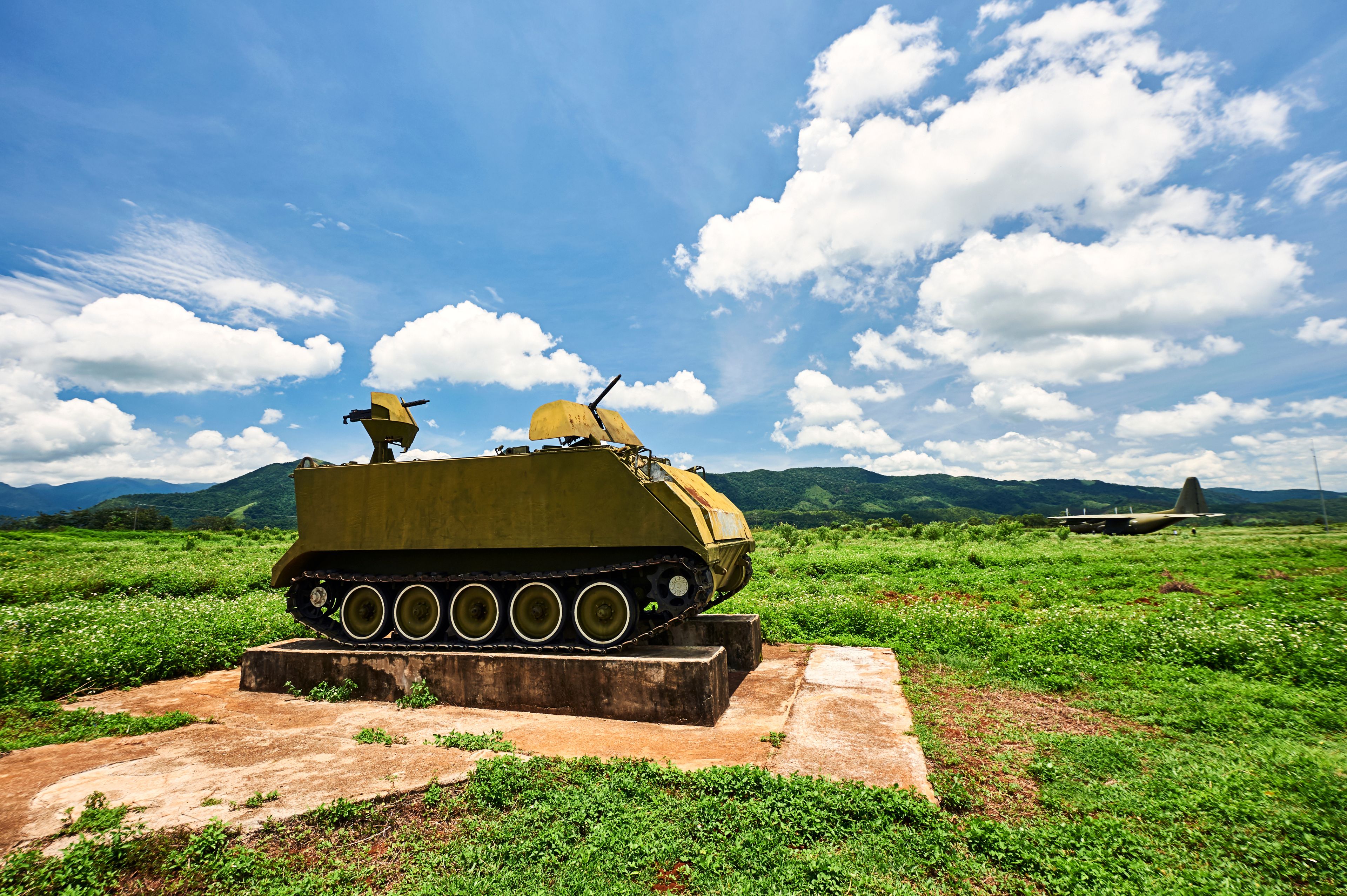 Un char d’assaut est exposé dans un champ verdoyant, avec des montagnes en arrière-plan.