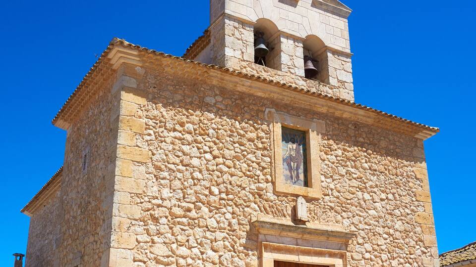 A stone church with a bell tower, a wooden door, and a red and white sign.