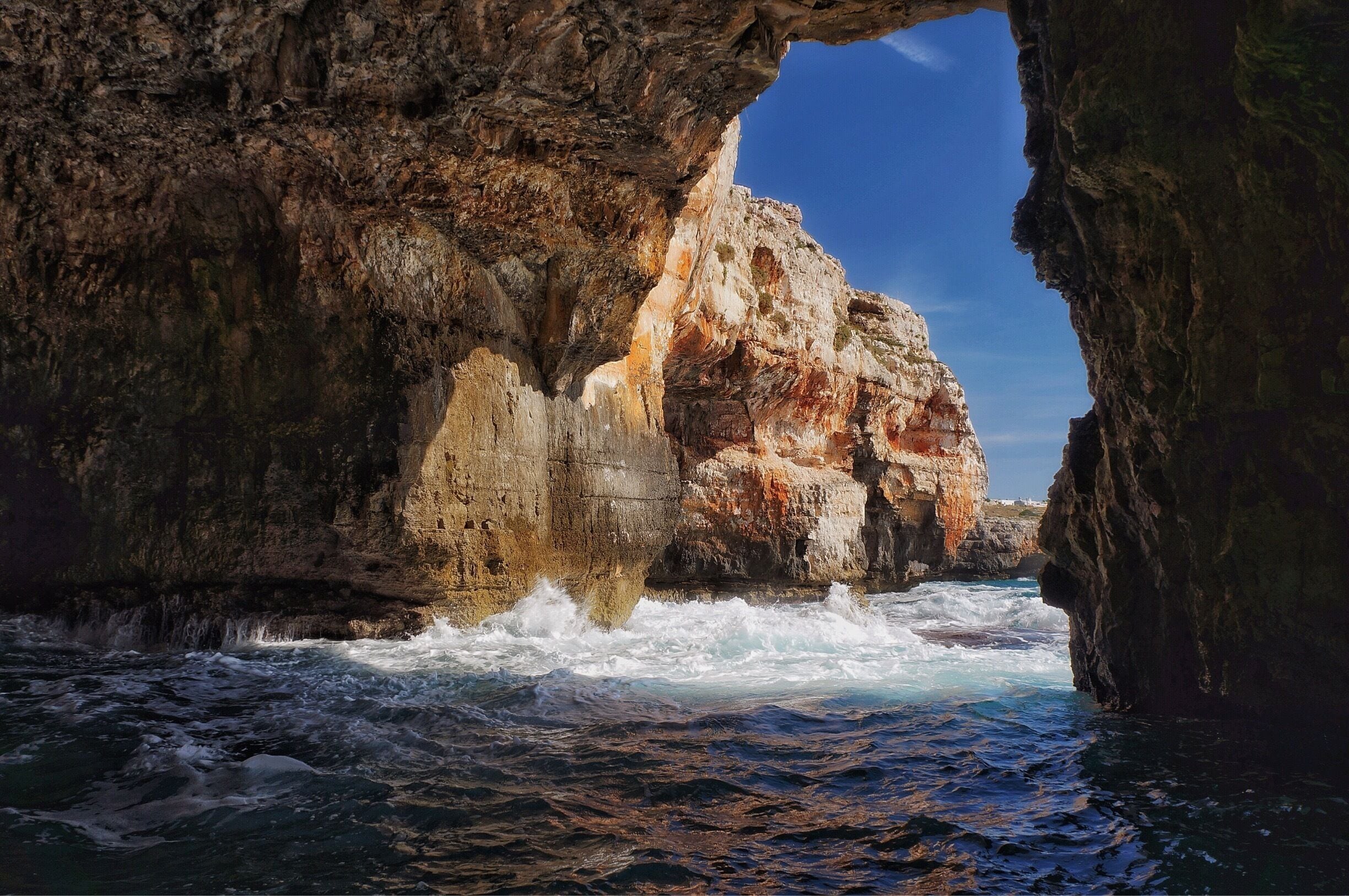 A rocky coastline with waves crashing against the shore and a cave entrance.