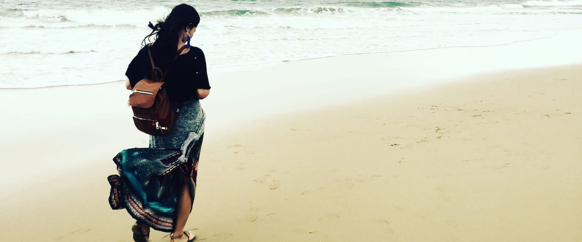 A person walking on a sandy beach with ocean waves in the background.