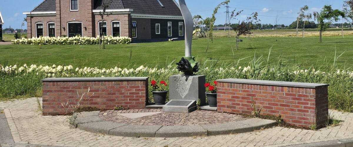 A brick house with a sloped roof, a tall metal sculpture, and a well-maintained lawn with white flowers.
