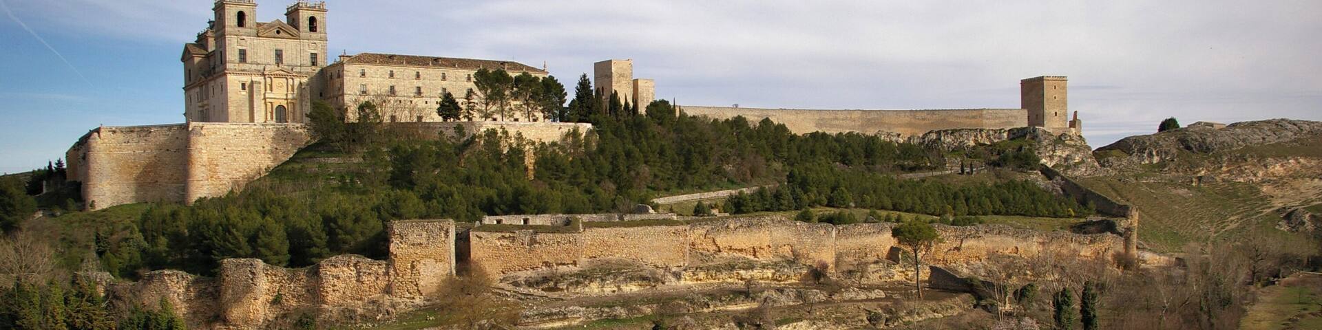 A historic castle on a hill with surrounding ruins and a sports field.