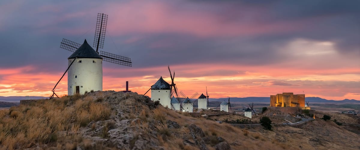 Windmills, a castle, and a sunset over a hilly landscape.