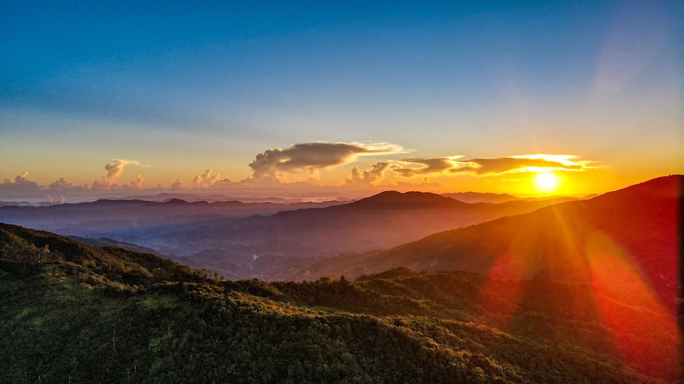 A mountain landscape at sunset with the sun setting behind the hills.