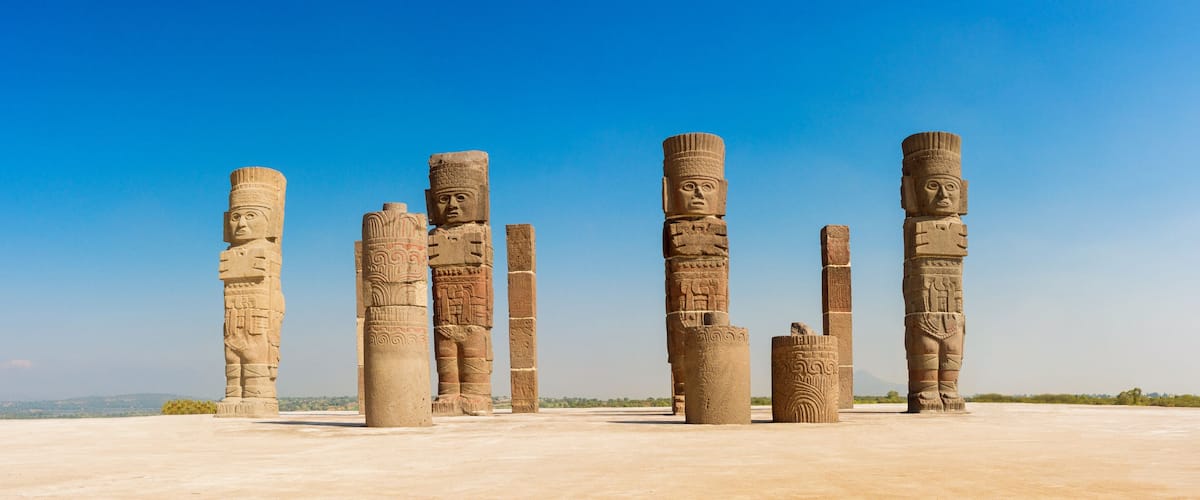 Ancient stone columns with intricate carvings, set against a clear blue sky.