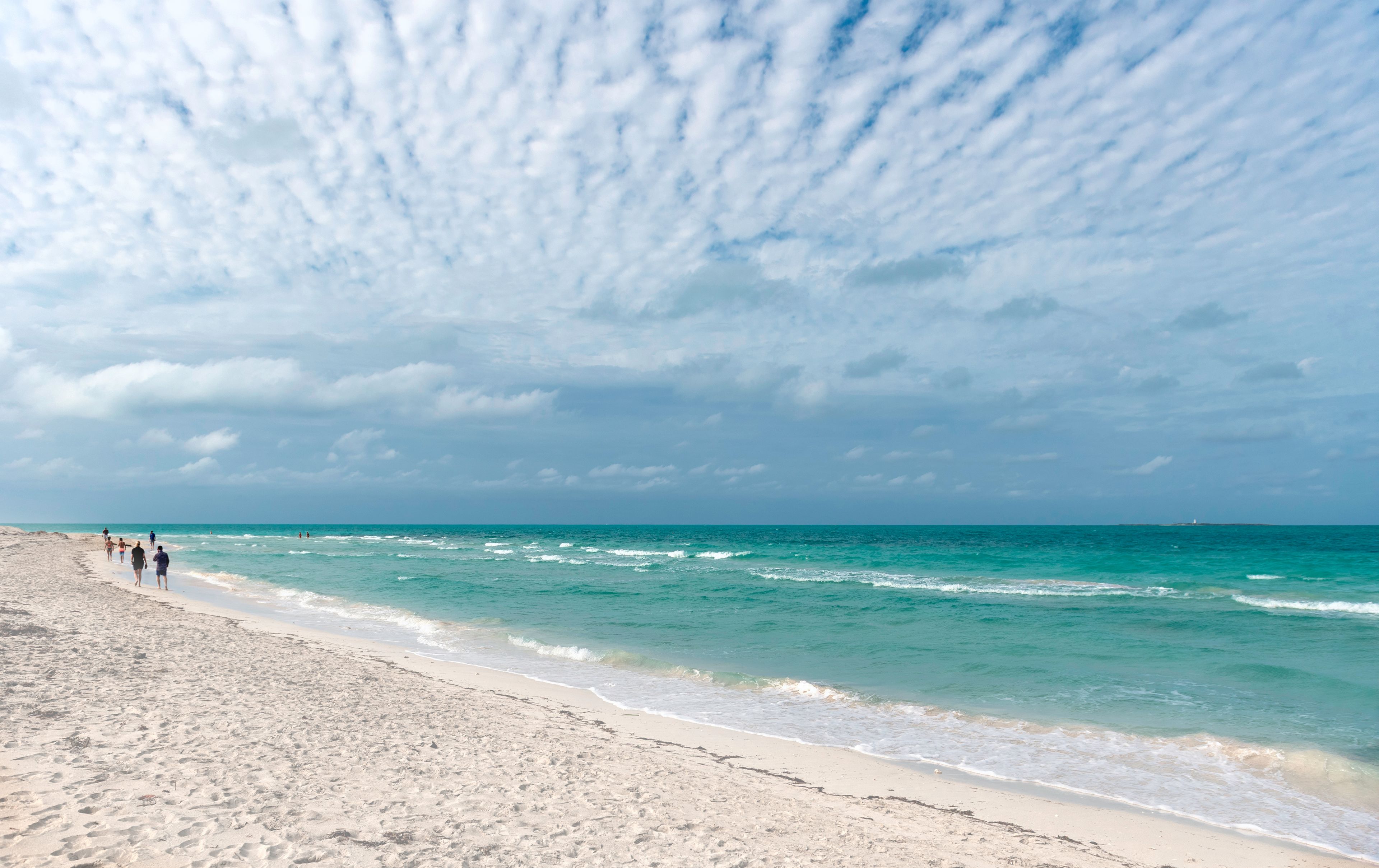 A beach with people walking along the shore, the ocean, and a cloudy sky.