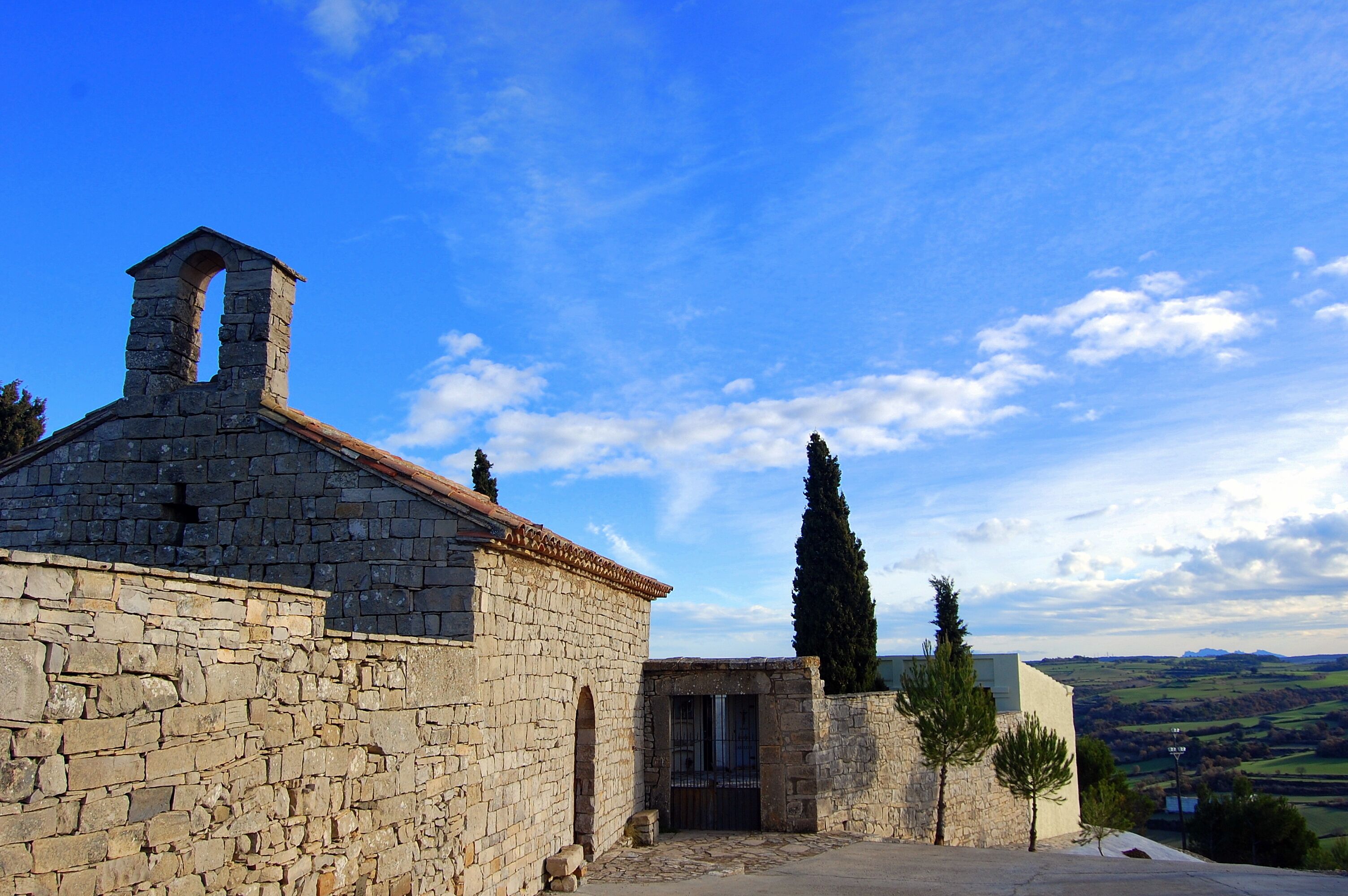 A stone building with a bell tower, a gate, and a view of the countryside.