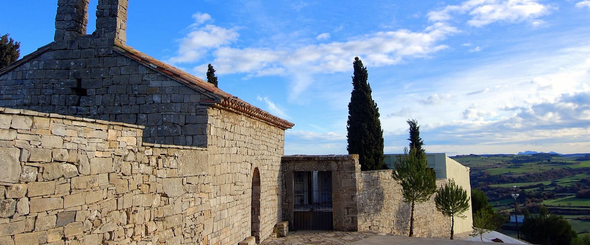 A stone building with a bell tower, a gate, and a view of the countryside.