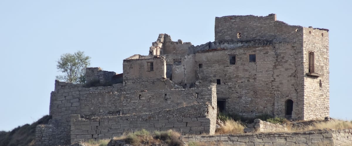 An ancient stone fortress with multiple towers and walls, surrounded by dry grass and sparse vegetation.