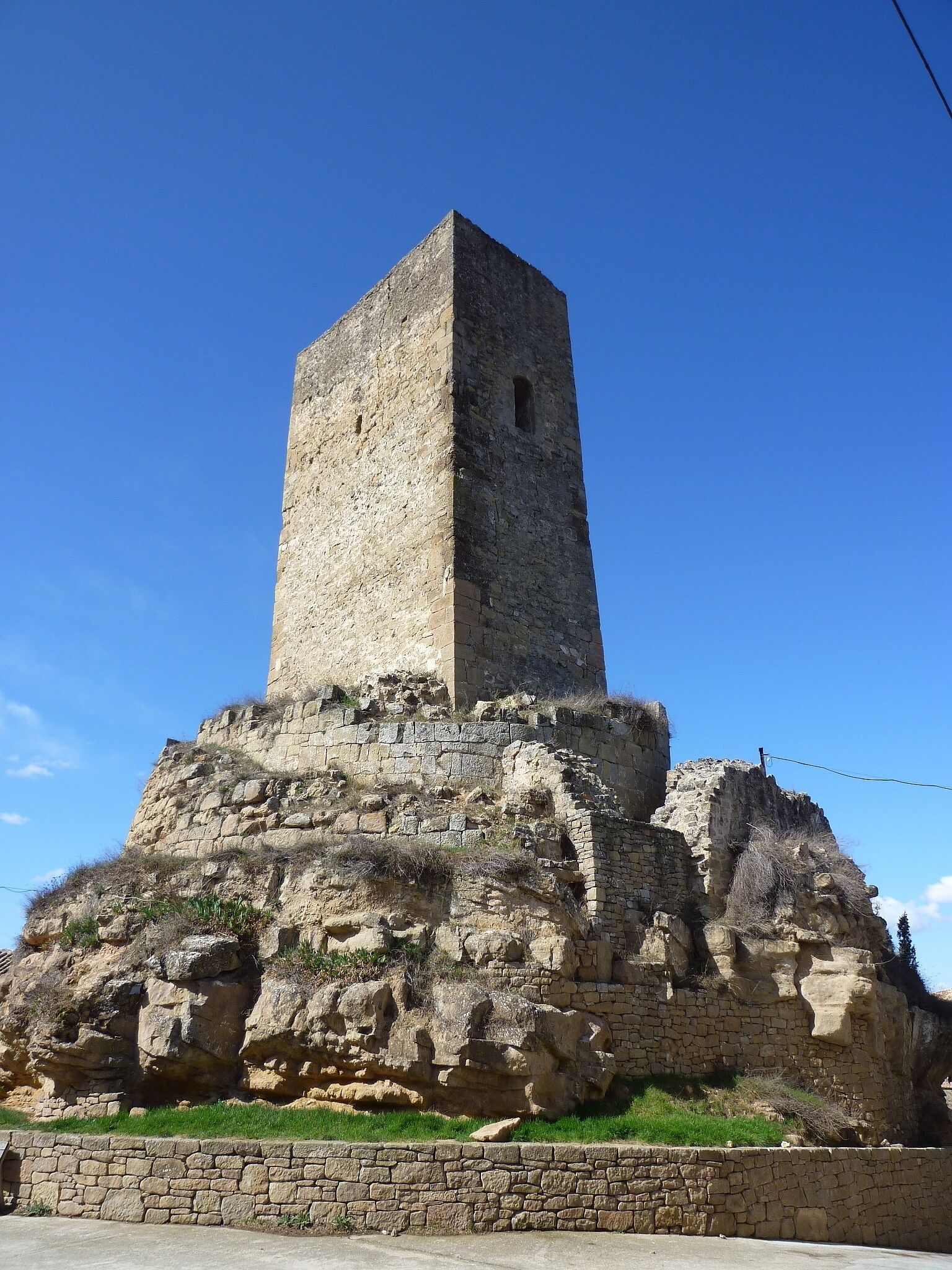 A tall, ancient stone tower with a square base, surrounded by ruins and greenery.