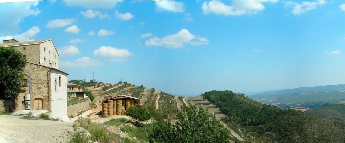 A rural landscape with a winding road, a stone building, and rolling hills under a clear sky.