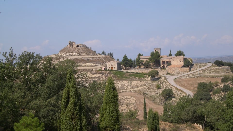 A historical site with ruins, a hilltop structure, and a building with arches.