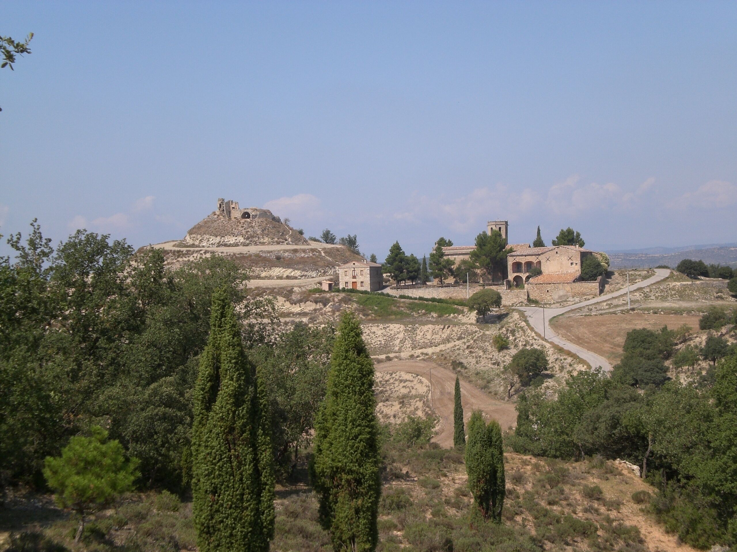 A historical site with ruins, a hilltop structure, and a building with arches.