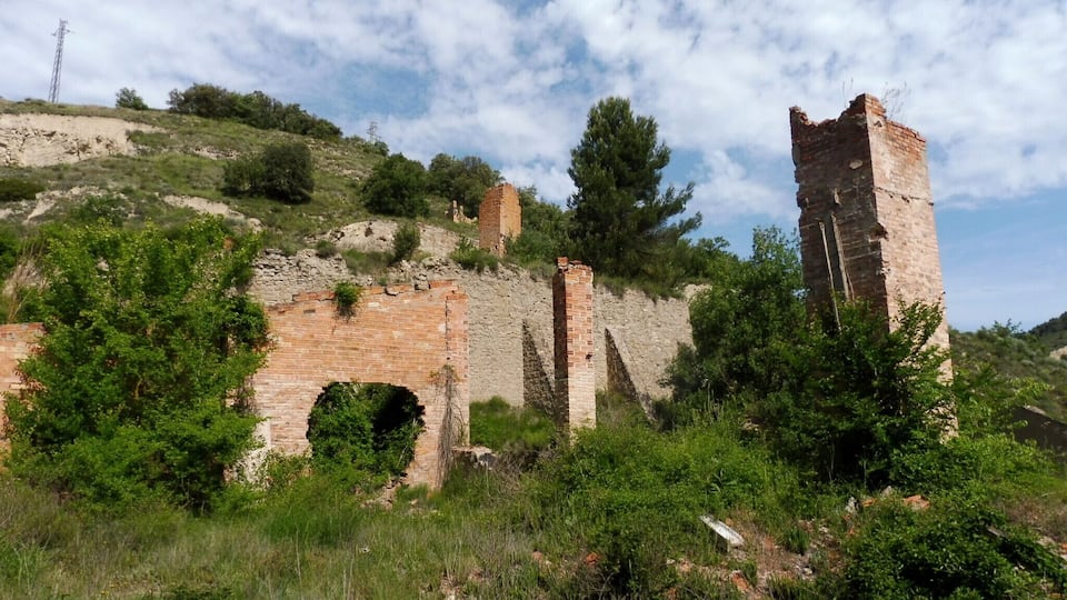 Ancient brick ruins on a hillside with greenery and a power line in the background.