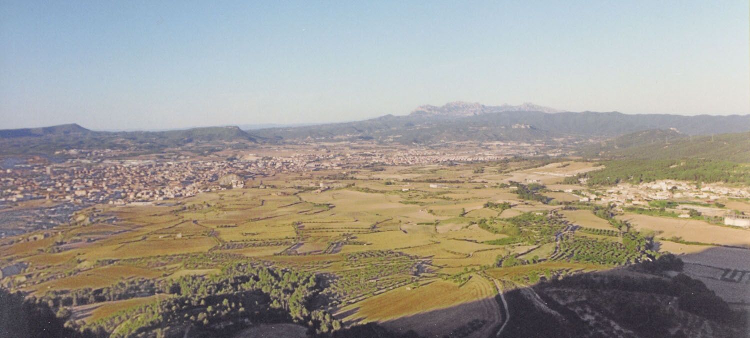 A panoramic view of a city surrounded by agricultural fields and distant mountains.