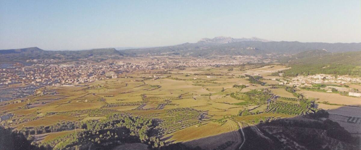 A panoramic view of a city surrounded by agricultural fields and distant mountains.