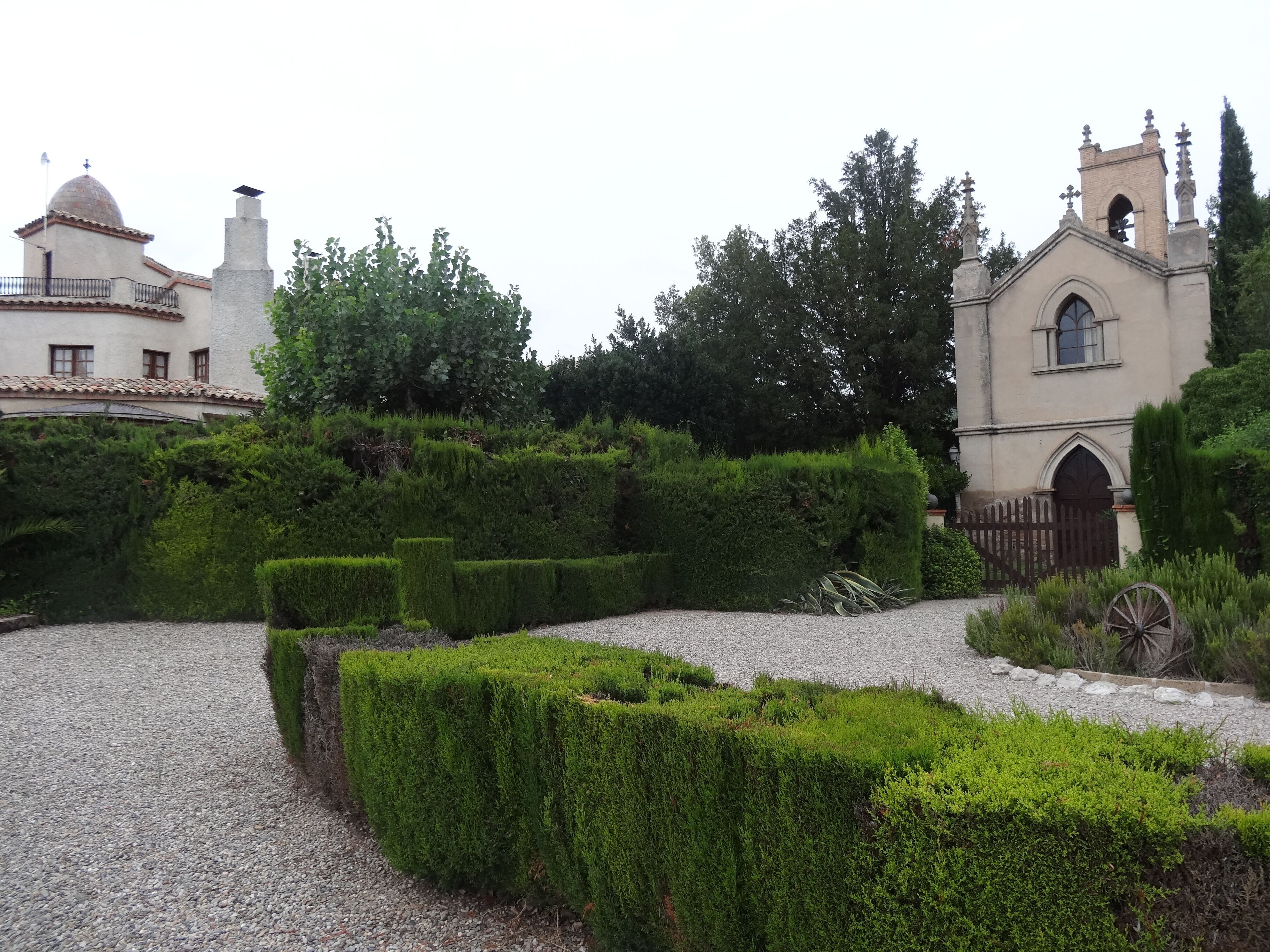 A formal garden with neatly trimmed hedges, a gravel path, and a historic building with a bell tower.