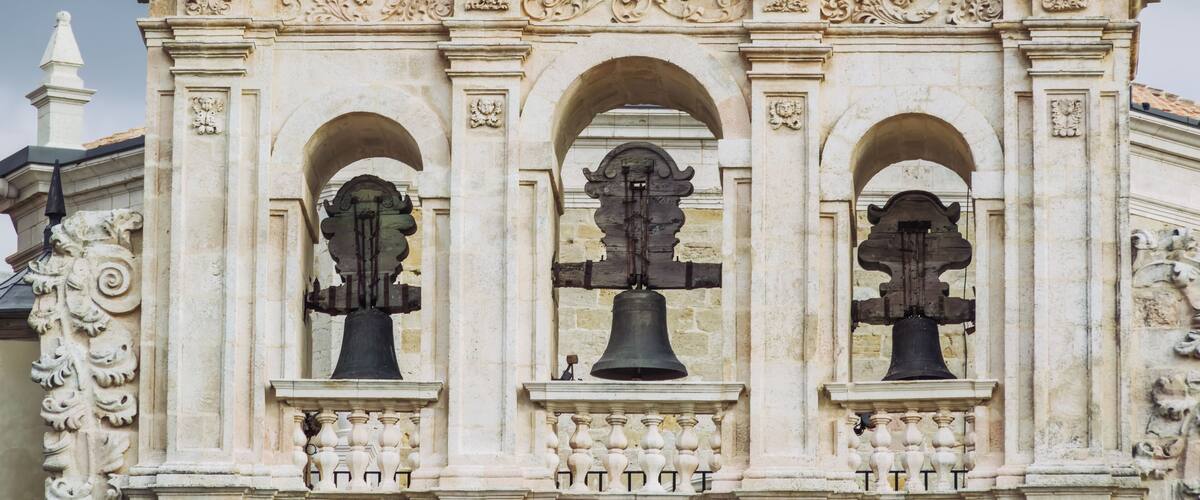 A historic building with ornate carvings and three large bells.