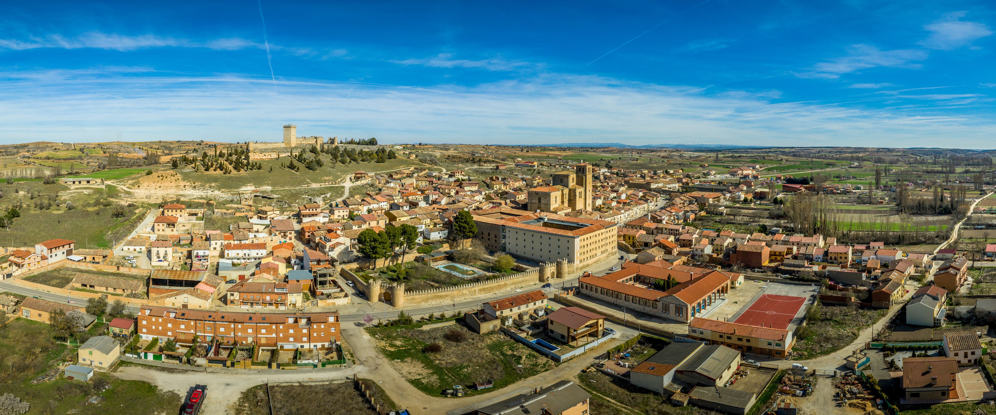 An aerial view of a historic town with a prominent castle, a central church, and surrounding residential buildings.