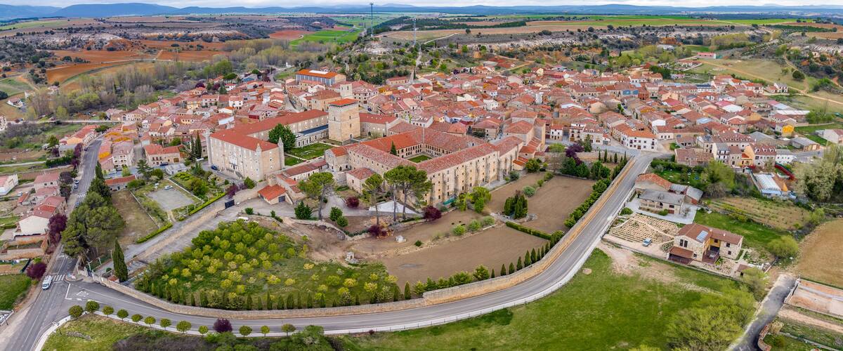 An aerial view of a historic town with red-roofed buildings, a central church, and surrounding fields.