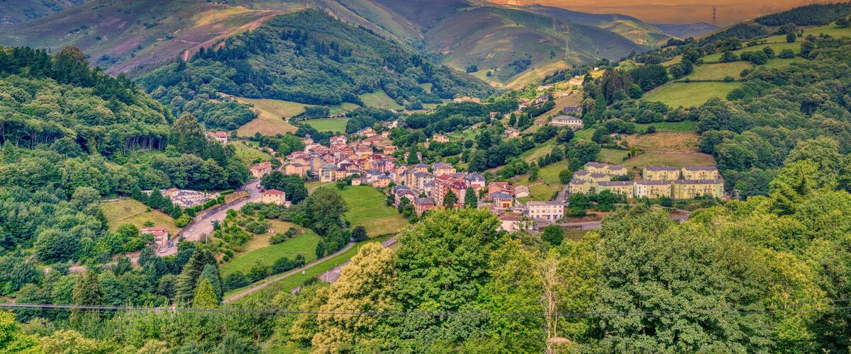 A village nestled in a valley surrounded by hills, with a prominent building in the center.